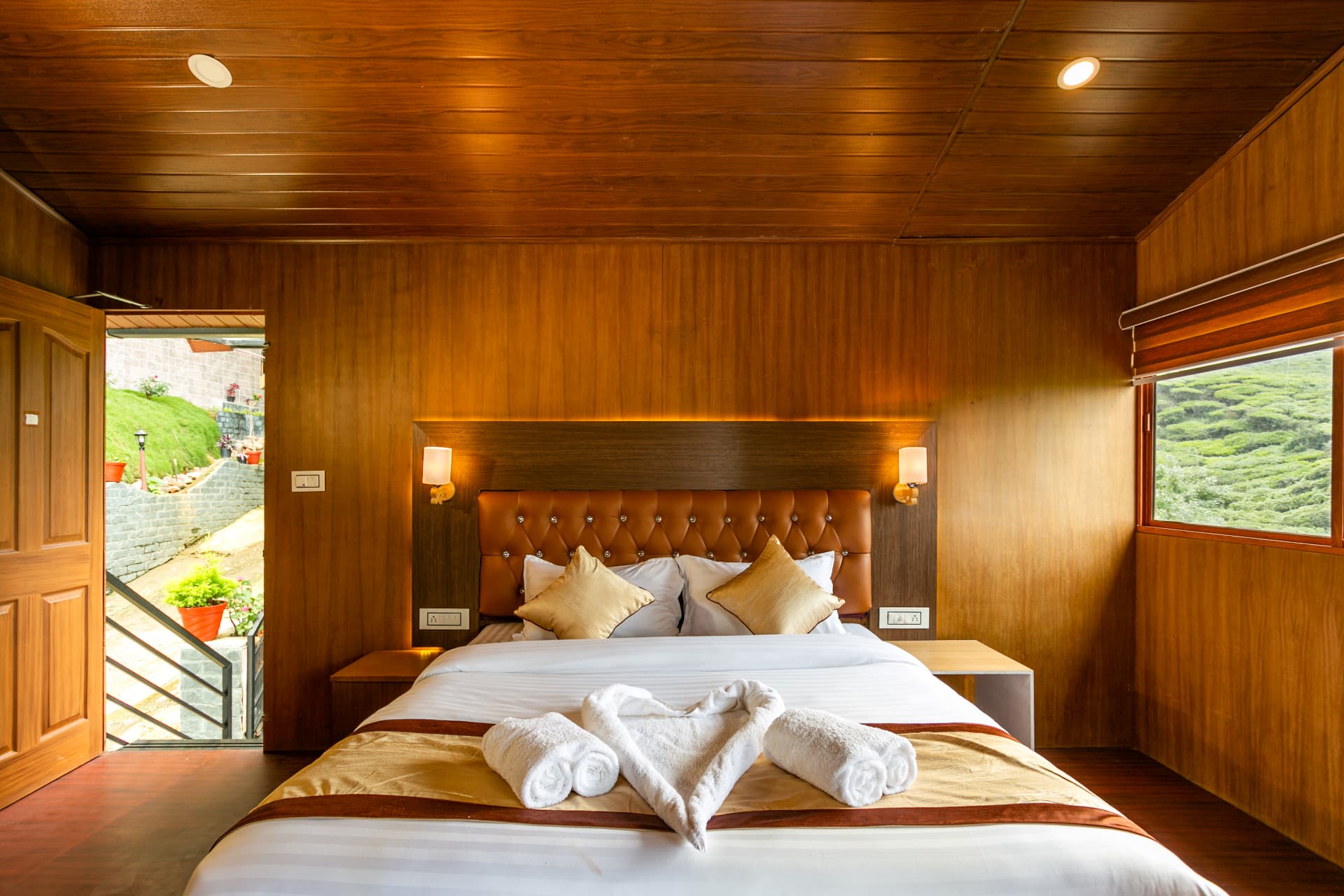 Premium Valley View Hut at Grand Valley Resort Munnar — teak-panelled room with king bed, garden door and a window onto the tea plantation