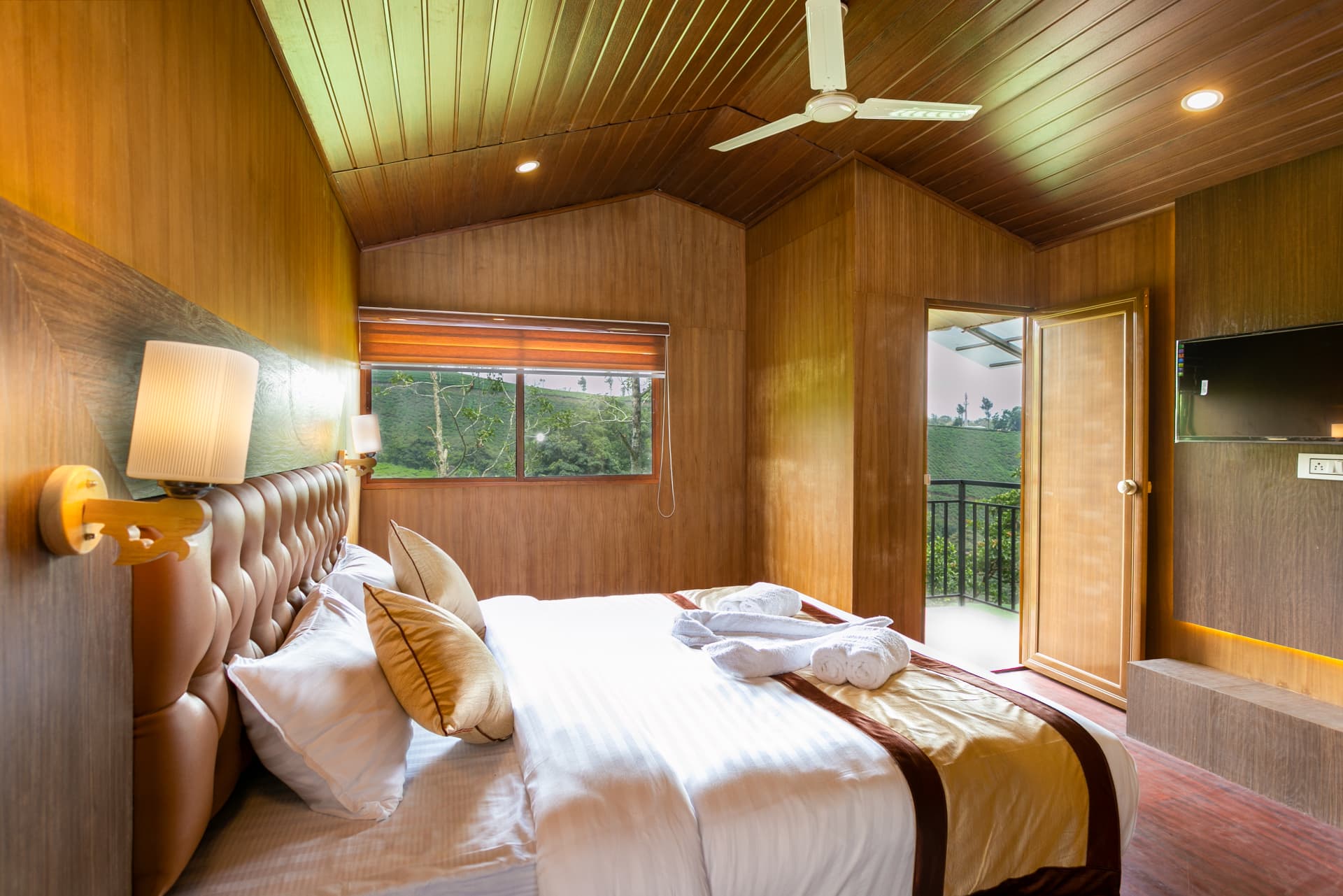 Premium Valley View Hut interior under a pitched wooden ceiling, balcony door open to the tea slope